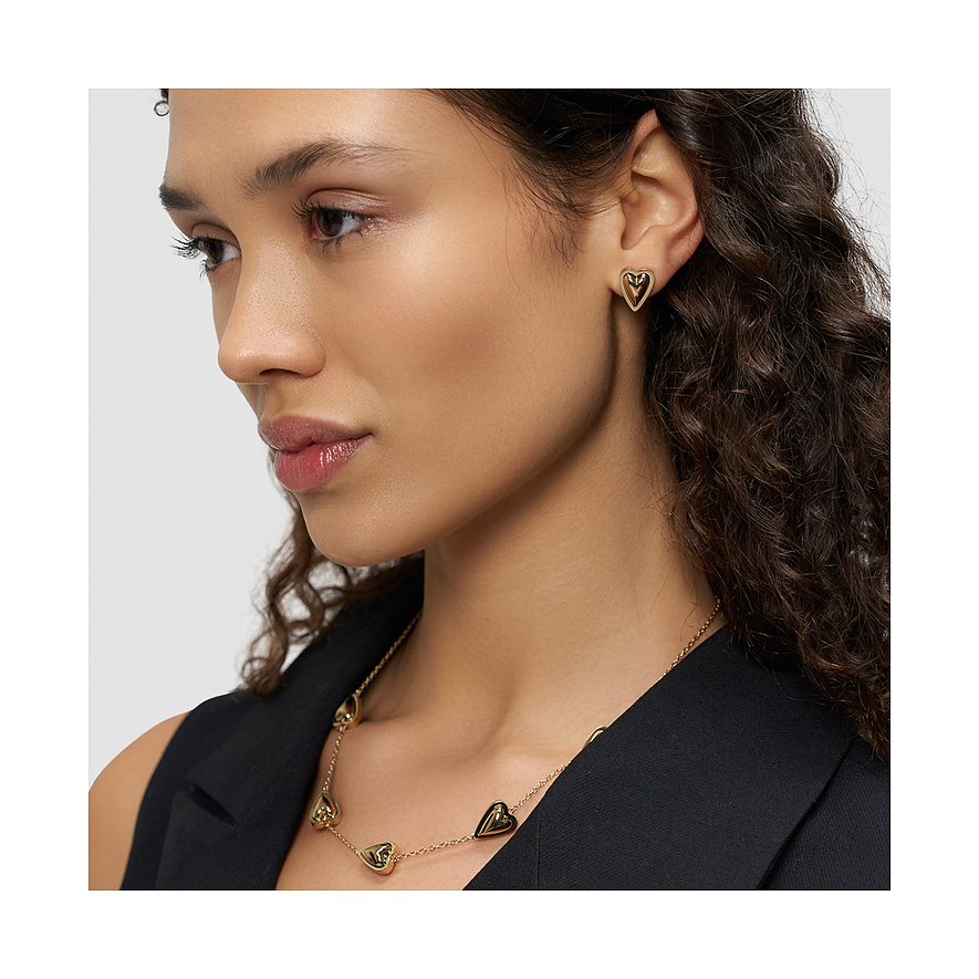 Model trägt Liebeskind Ohrschmuck aus gelbvergoldetem Edelstahl, herzförmige Ohrstecker und passende Halskette.