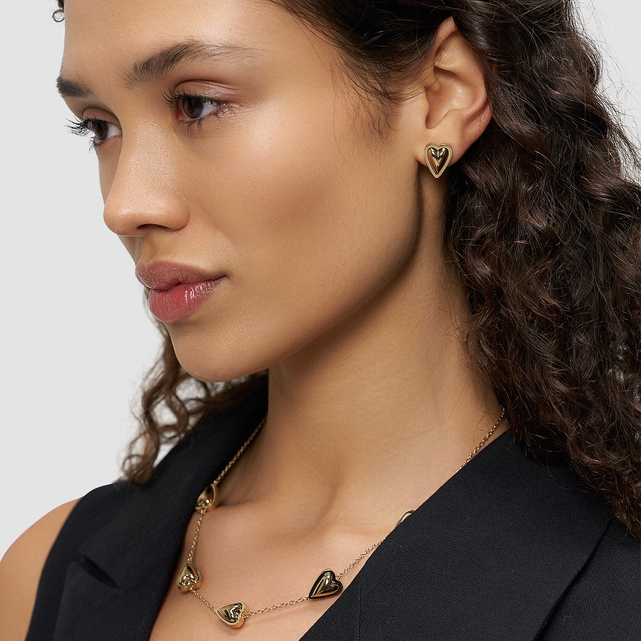 Model trägt Liebeskind Ohrschmuck aus gelbvergoldetem Edelstahl, herzförmige Ohrstecker und passende Halskette.