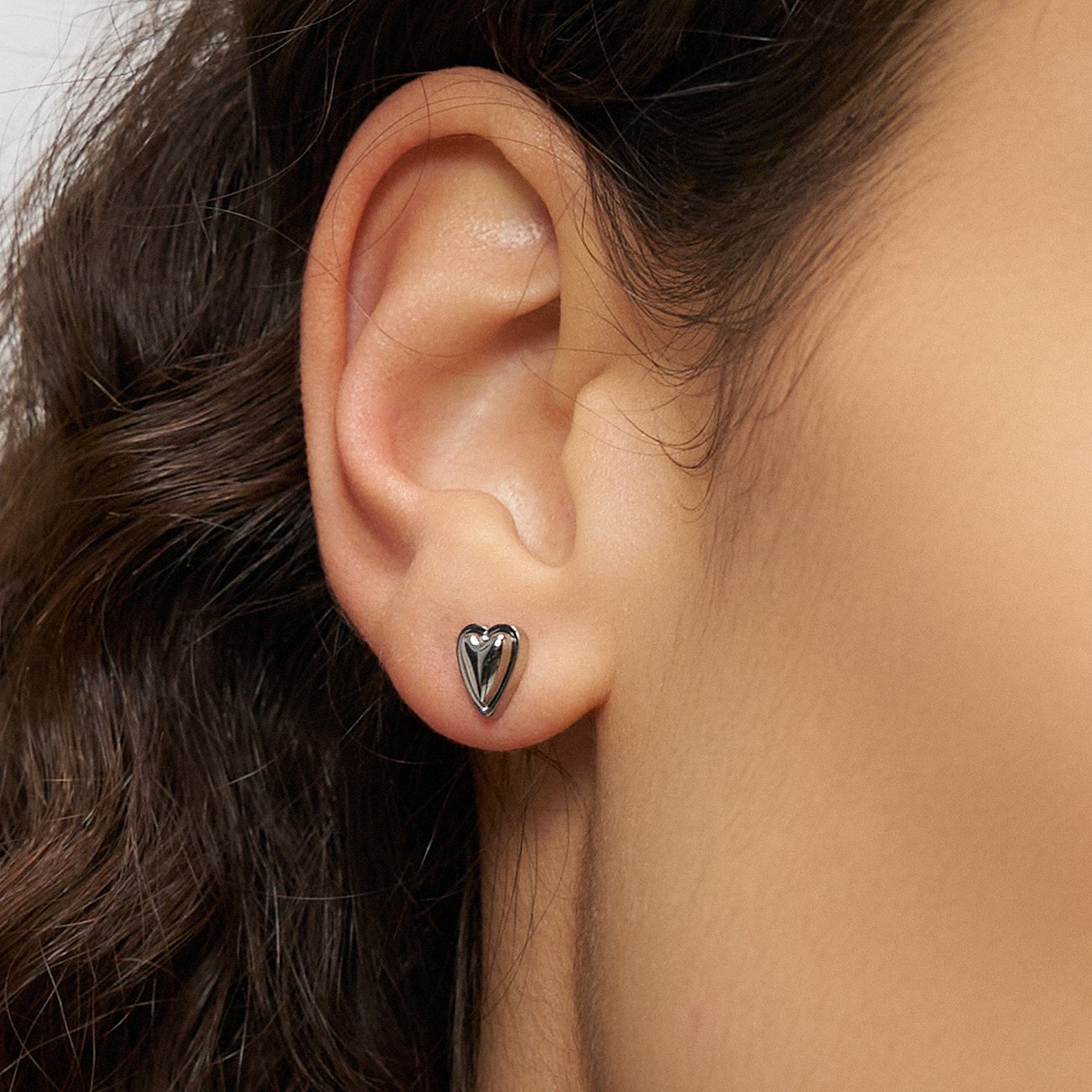 Nahaufnahme eines Ohres, das einen kleinen, herzförmigen Ohrstecker aus Edelstahl von Liebeskind trägt.