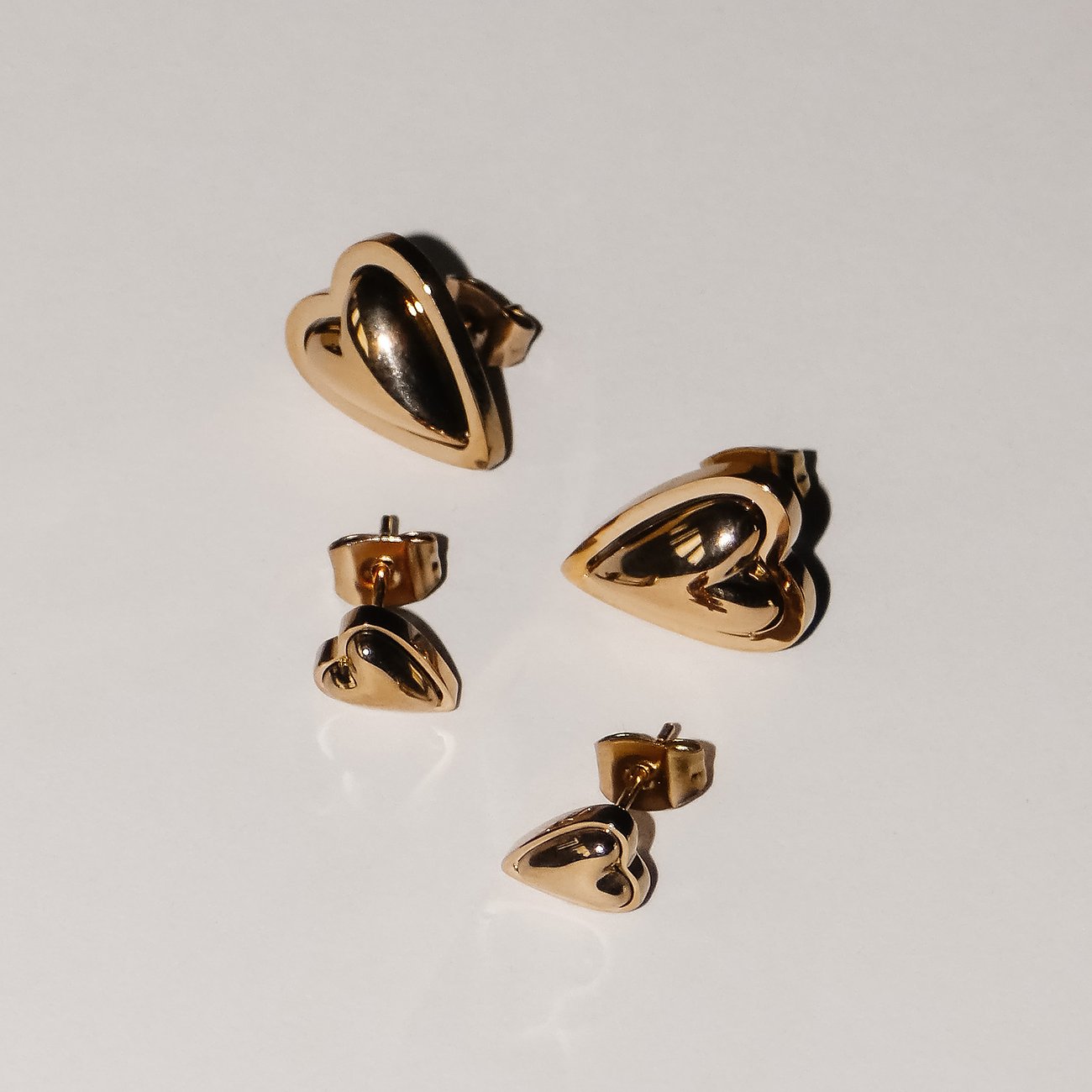 Liebeskind Ohrstecker aus goldfarbenem Edelstahl in Herzform in unterschiedlichen Größen auf einer Fläche.