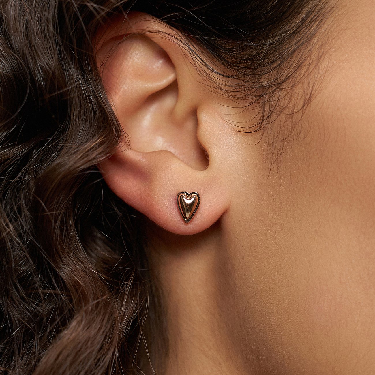 Nahaufnahme: rechtes Ohr eines Models mit herzförmigem Liebeskind Ohrstecker aus rosegoldfarbenem Edelstahl.