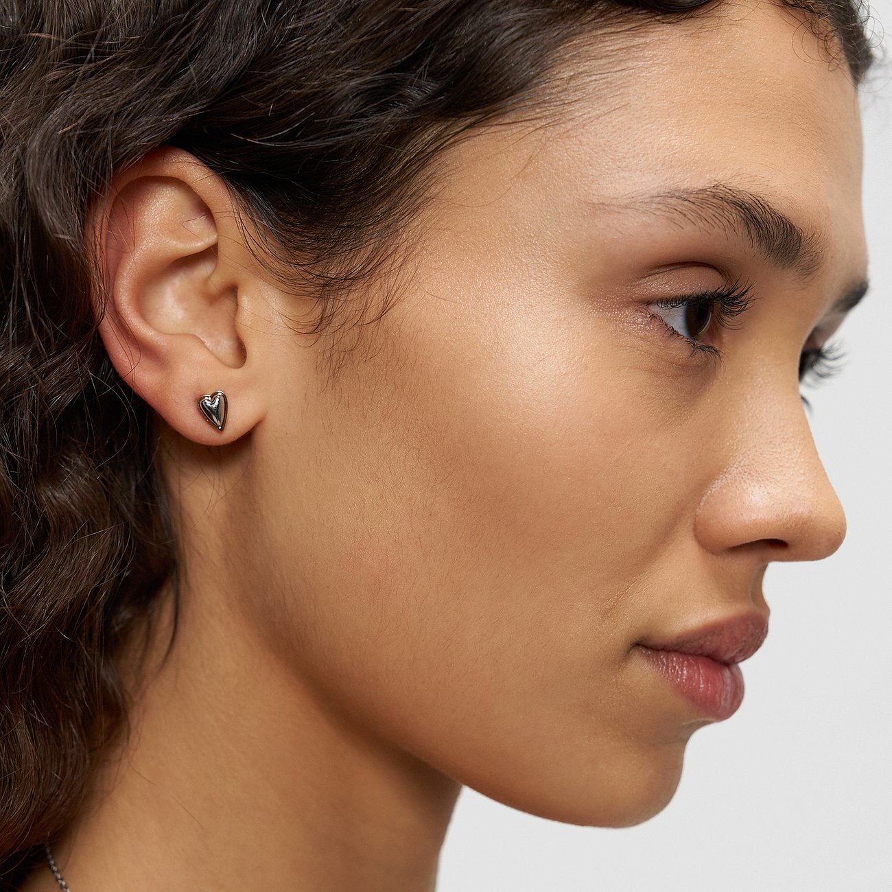 Nahaufnahme einer Person mit einem kleinen, glänzenden, herzförmigen Ohrstecker aus Liebeskind Edelstahl am rechten Ohr.