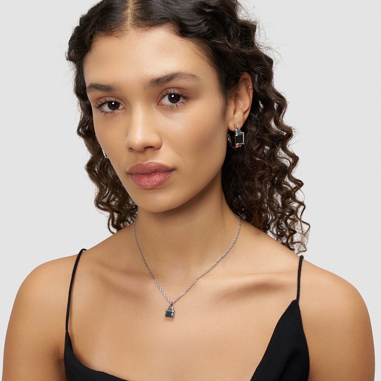 Une femme porte un collier Liebeskind en acier inoxydable avec un pendentif carré foncé.