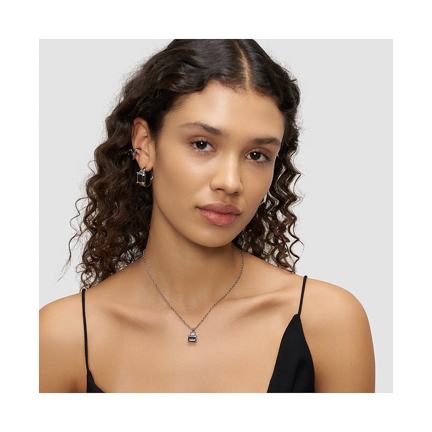 Une femme aux boucles marron foncé porte un collier Liebeskind en acier inoxydable avec un pendentif sombre.