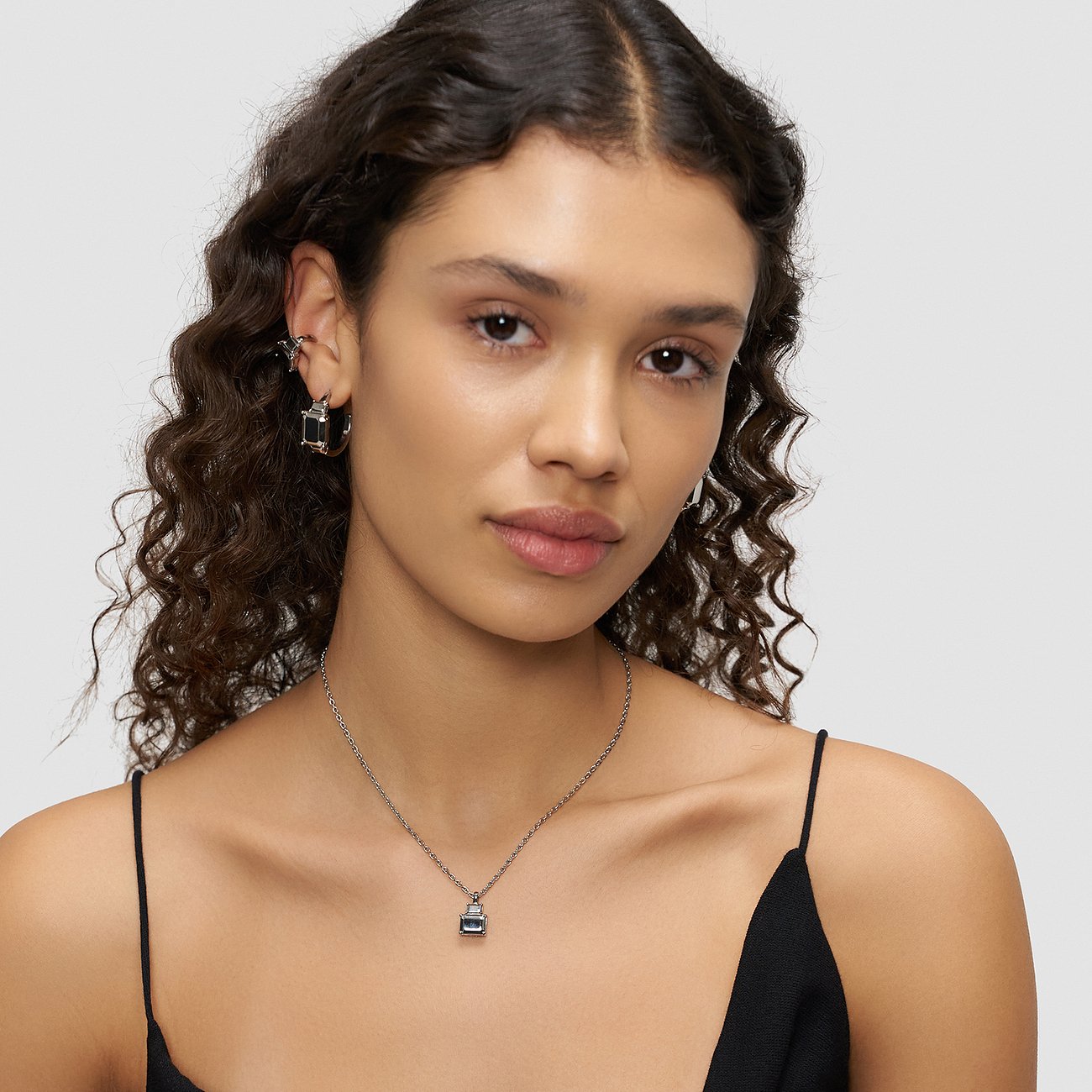 Une femme aux boucles marron foncé porte un collier Liebeskind en acier inoxydable avec un pendentif sombre.