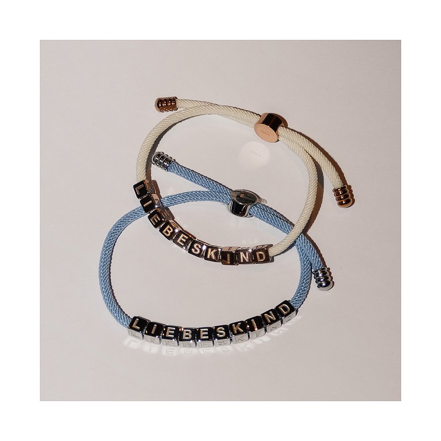 Zwei Liebeskind-Armbänder aus Edelstahl und Textil, eines hellblau und eines cremefarben, nebeneinander liegend.
