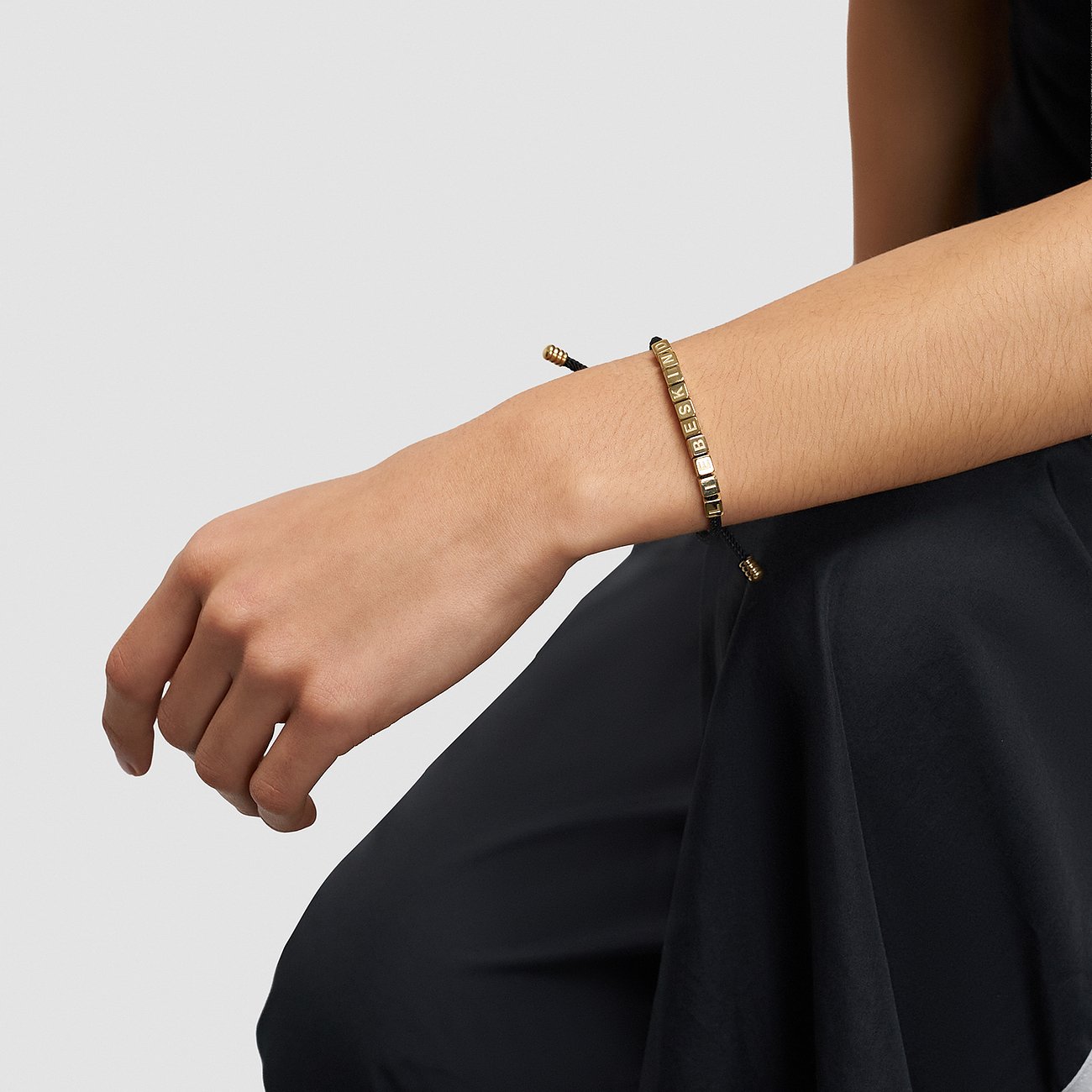 Am Handgelenk getragenes Liebeskind Armband aus Edelstahl mit goldenen Beads, die das Wort ‘LIEBESKIND’ bilden.