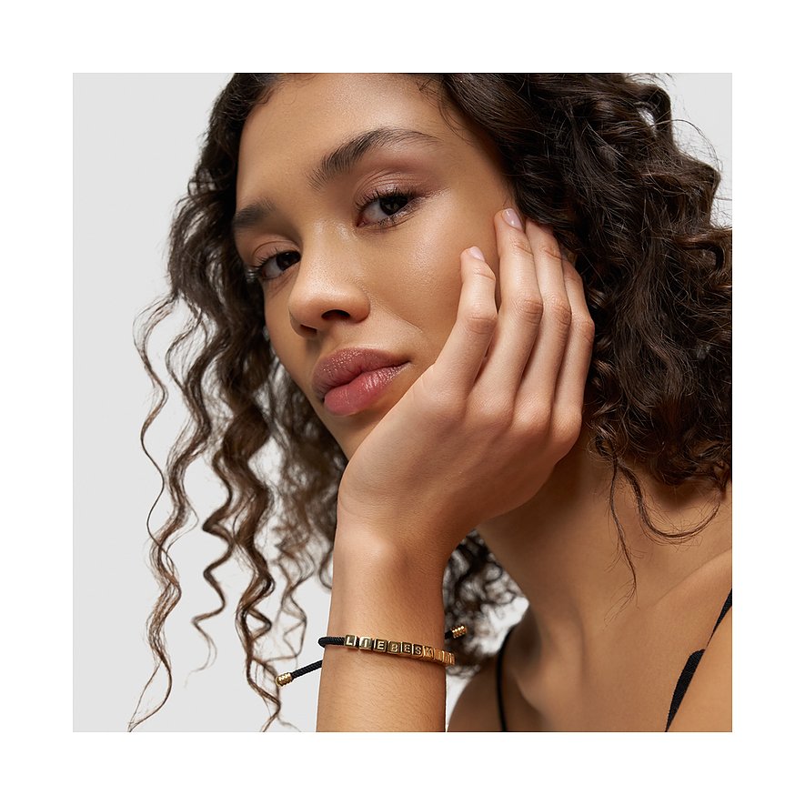 Ein Liebeskind Armschmuck aus Edelstahl mit goldfarbenen Würfelperlen zeigt „LIEBESKIND“ geschrieben am Handgelenk.