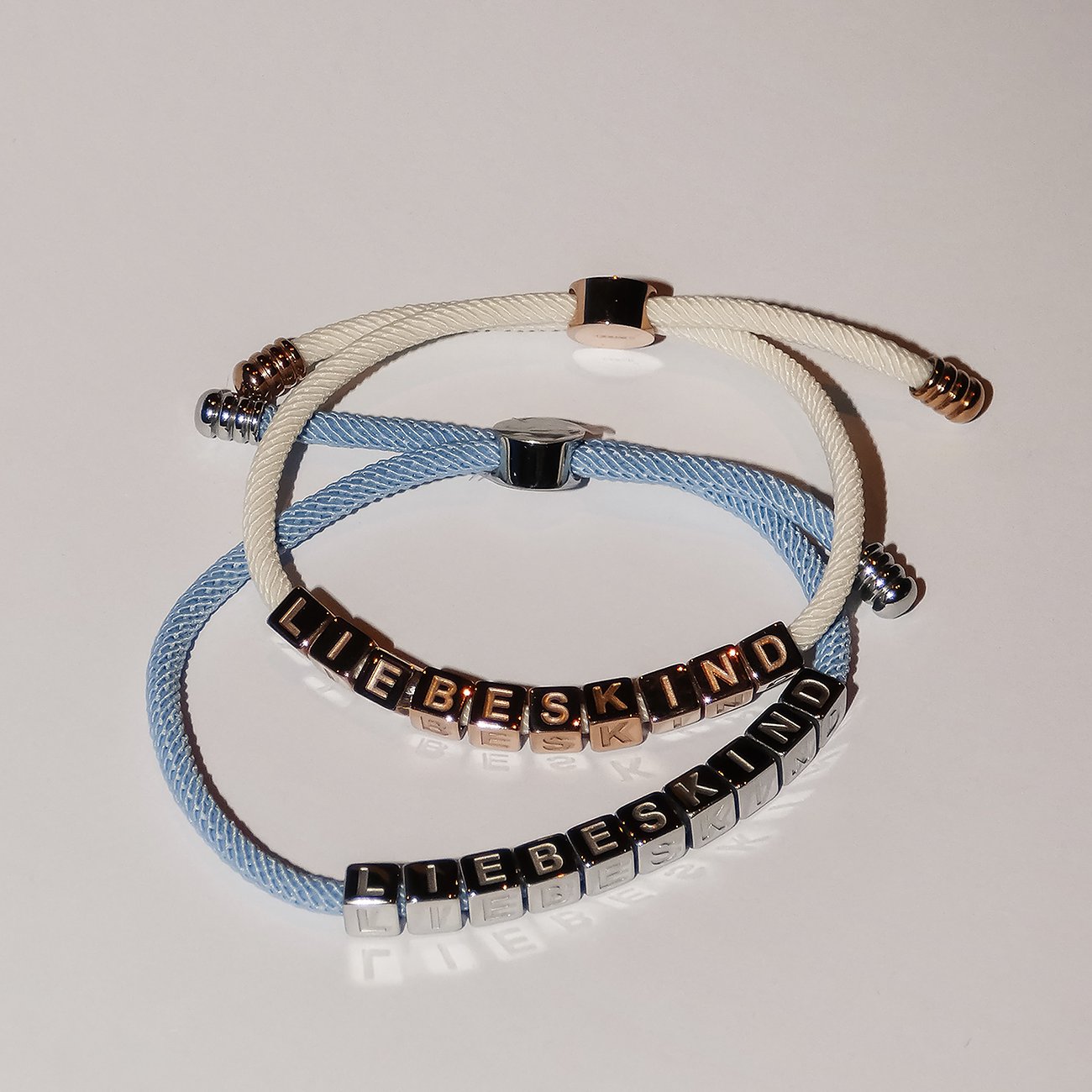 Zwei Liebeskind Edelstahl-Armbänder überkreuzt. Hellblau mit silbernen, creme-weiß mit roségoldenen Buchstaben.