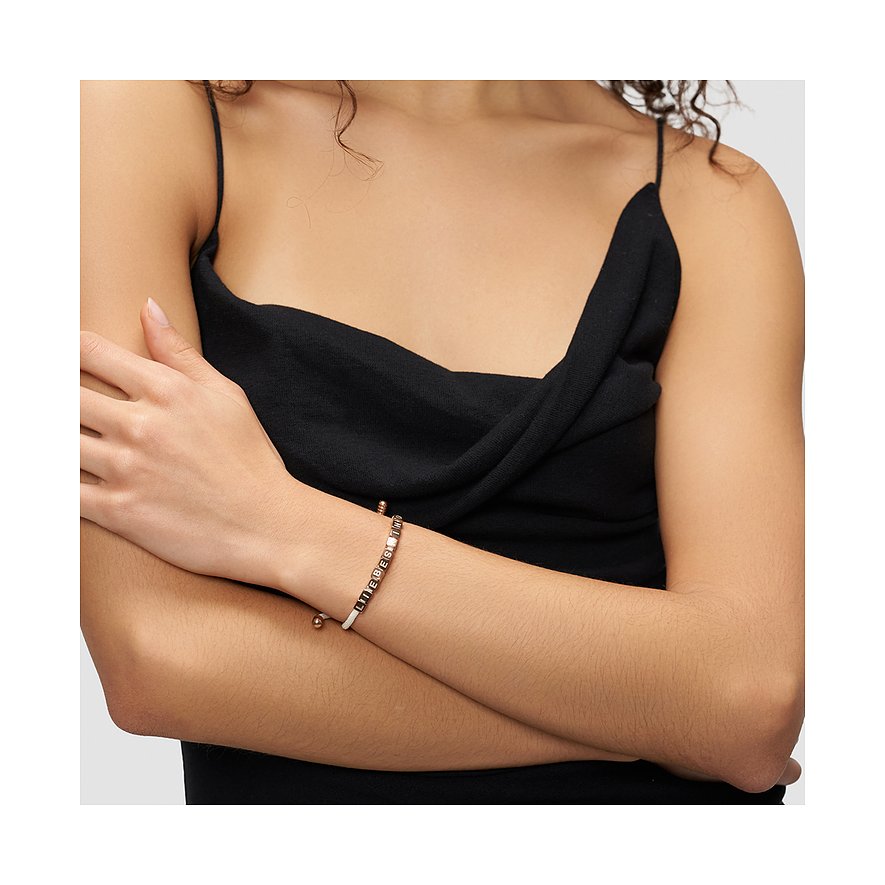 Frau trägt Liebeskind Edelstahl-Armband mit weißen/roségoldenen Perlen und eingeprägtem Schriftzug „LIEBE IST ALLES“.