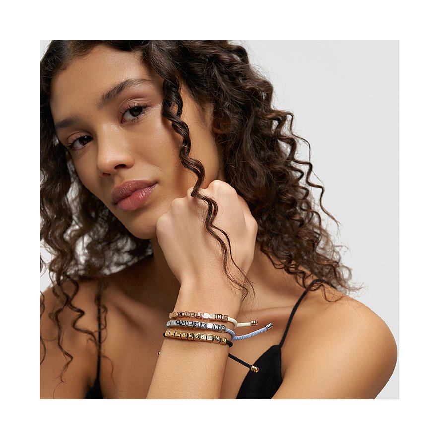 Nahaufnahme einer Frau, die drei Liebeskind Edelstahl Armschmuck Armbänder trägt, auf denen das Wort Liebeskind steht.
