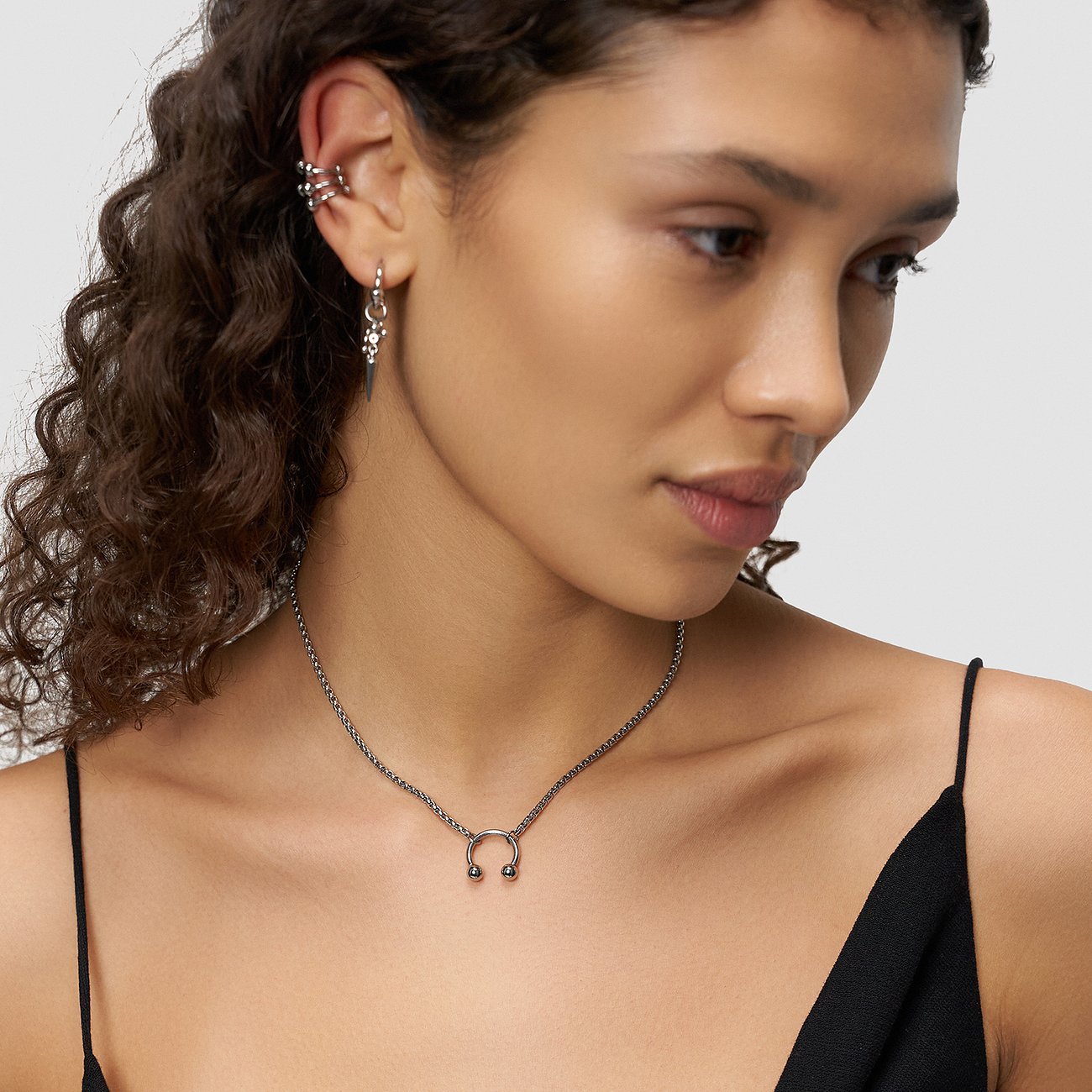 Model wears a Liebeskind necklace with a horseshoe pendant, matching earrings, and ear cuffs, all in shiny stainless steel.