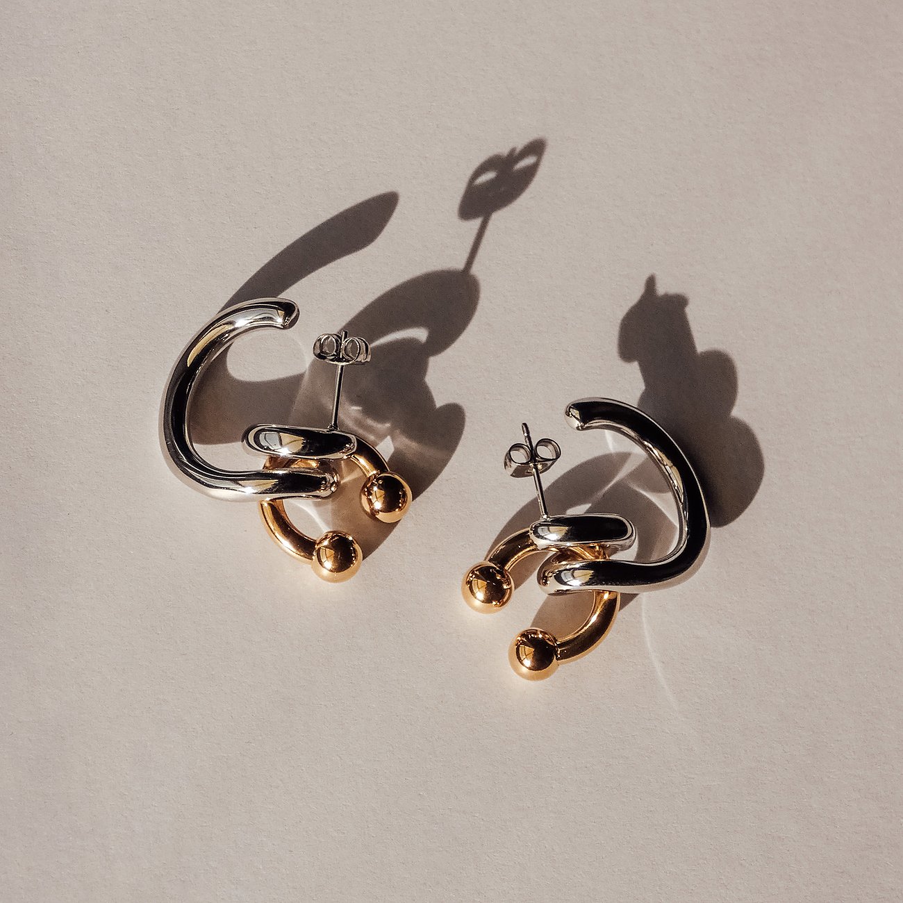 Ein Paar Ohrschmuck von Liebeskind aus Edelstahl, mit silber- und goldfarbenen C-förmigen Elementen und kleinen Kugeln.
