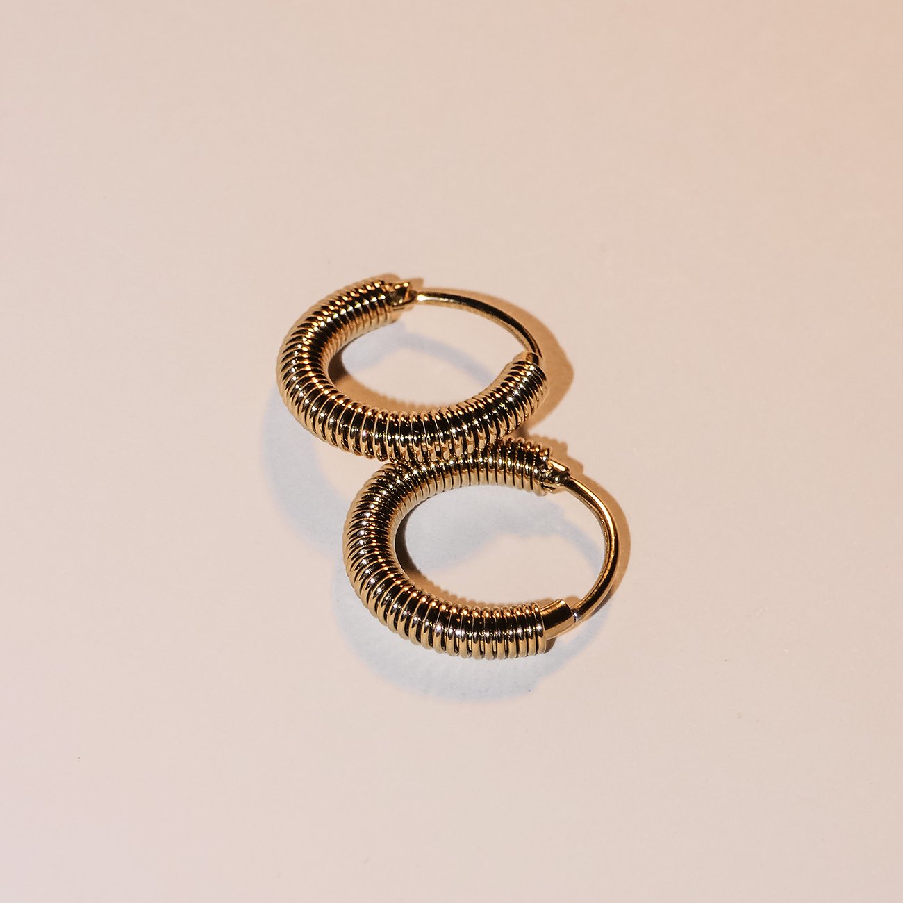 Boucles d'oreilles Liebeskind en acier inoxydable doré, finement rainurées et brillantes, photographiées du dessus.