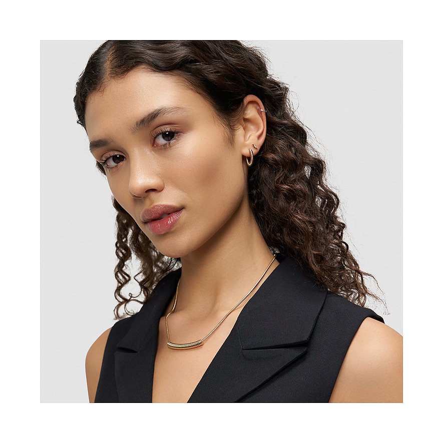 Le mannequin porte des boucles d'oreilles Liebeskind en acier inoxydable plaqué or, deux petits anneaux simples.