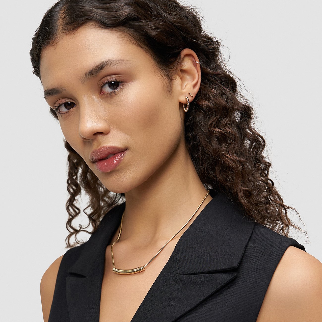 Le mannequin porte des boucles d'oreilles Liebeskind en acier inoxydable plaqué or, deux petits anneaux simples.