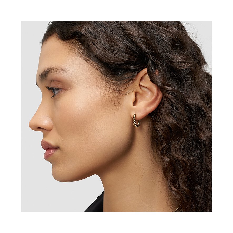 Gros plan d'une boucle d'oreille créole dorée Liebeskind en acier inoxydable sur une oreille.