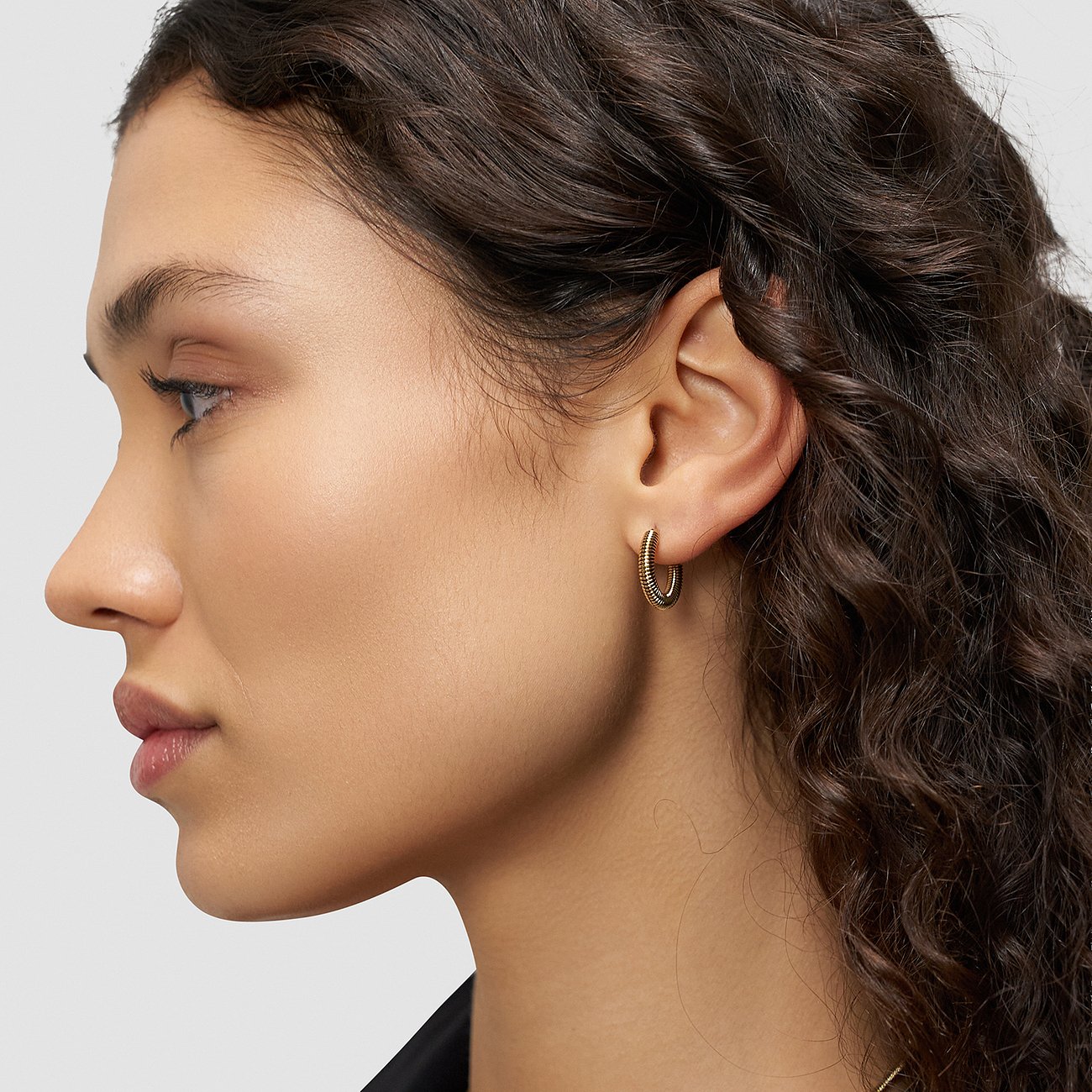 Gros plan d'une boucle d'oreille créole dorée Liebeskind en acier inoxydable sur une oreille.