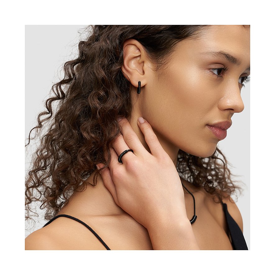 Gros plan d'une femme portant des boucles d'oreilles Liebeskind en acier inoxydable et une bague assortie.