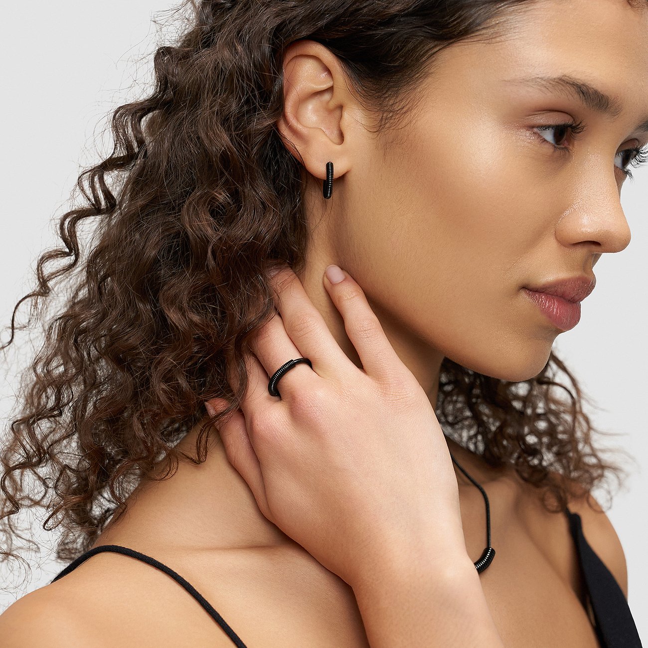Gros plan d'une femme portant des boucles d'oreilles Liebeskind en acier inoxydable et une bague assortie.