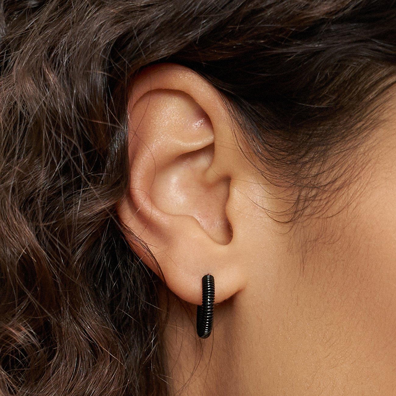 Gros plan d'une personne portant un bijou d'oreille Liebeskind noir en acier inoxydable, présentant une texture rainurée.