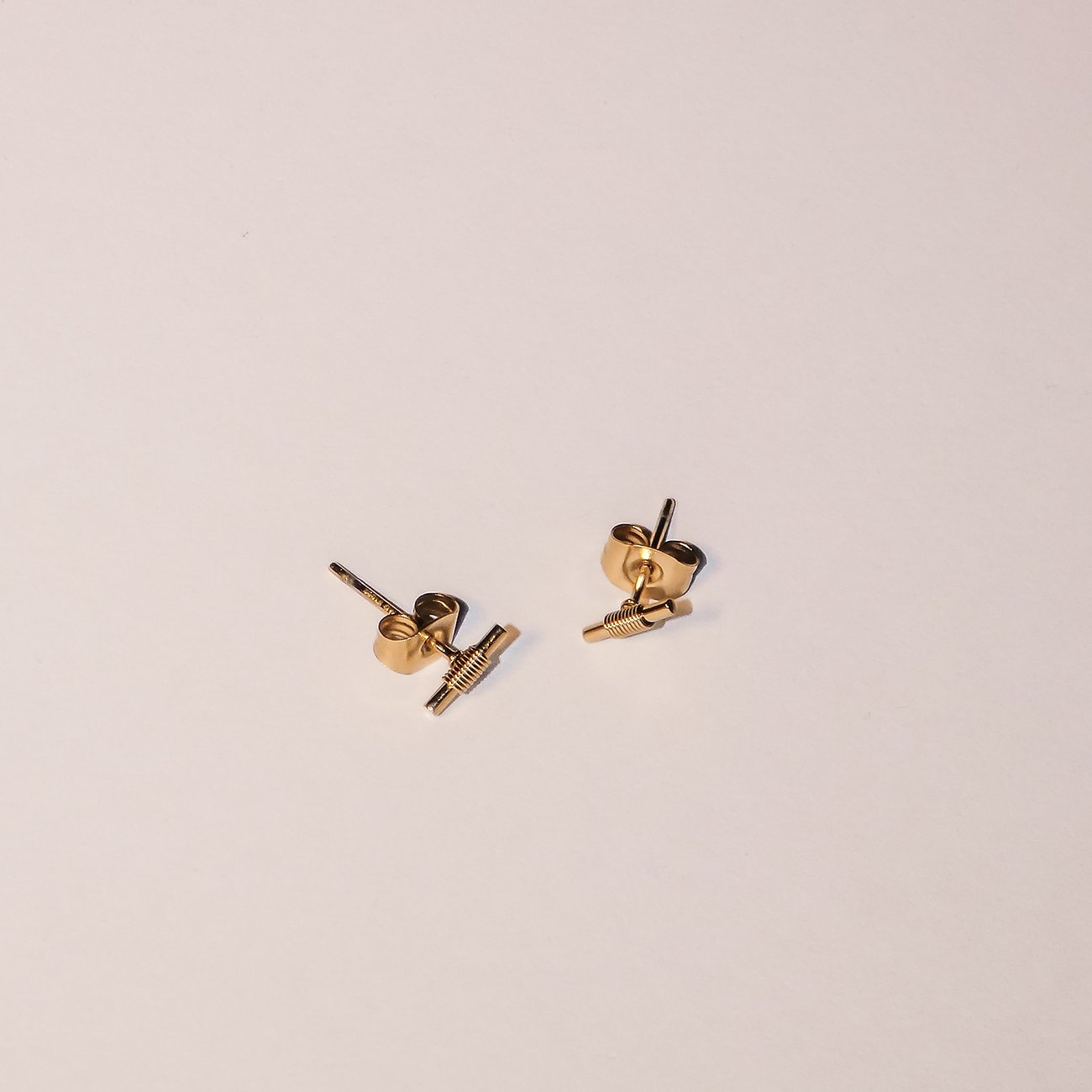 Liebeskind guld-ørrestikker i rustfrit stål, formet som små riflede stænger, på hvid baggrund.