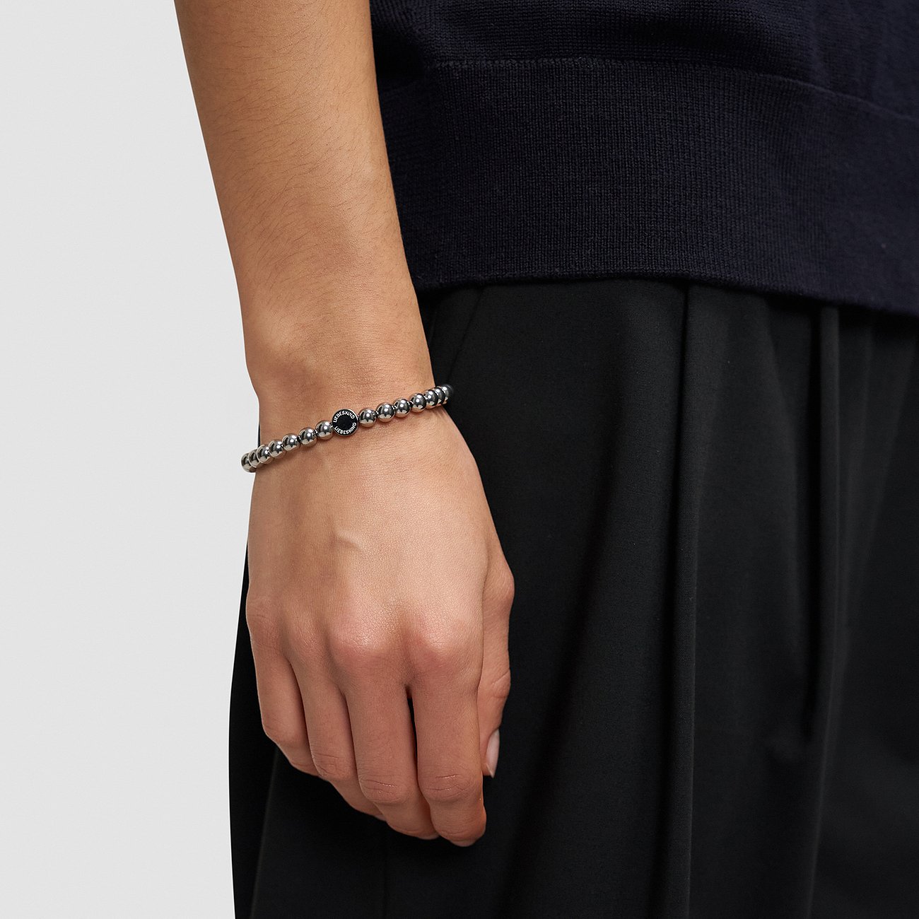 Liebeskind armband i rostfritt stål med glänsande kulor och ett svart mittelelement, buret på en handled.