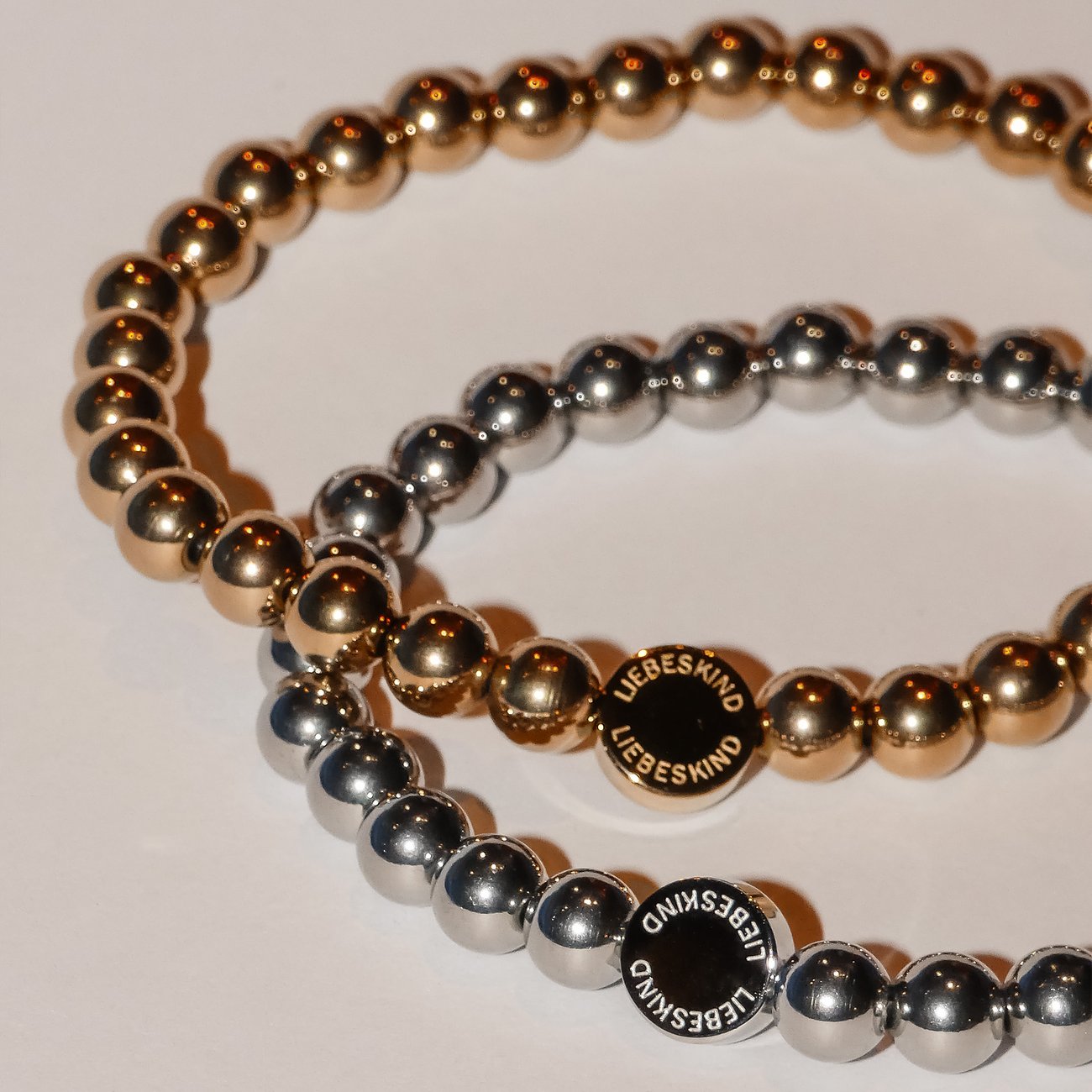 Två Liebeskind-armband i rostfritt stål med små kulor, ett guldfärgat och ett silverfärgat.