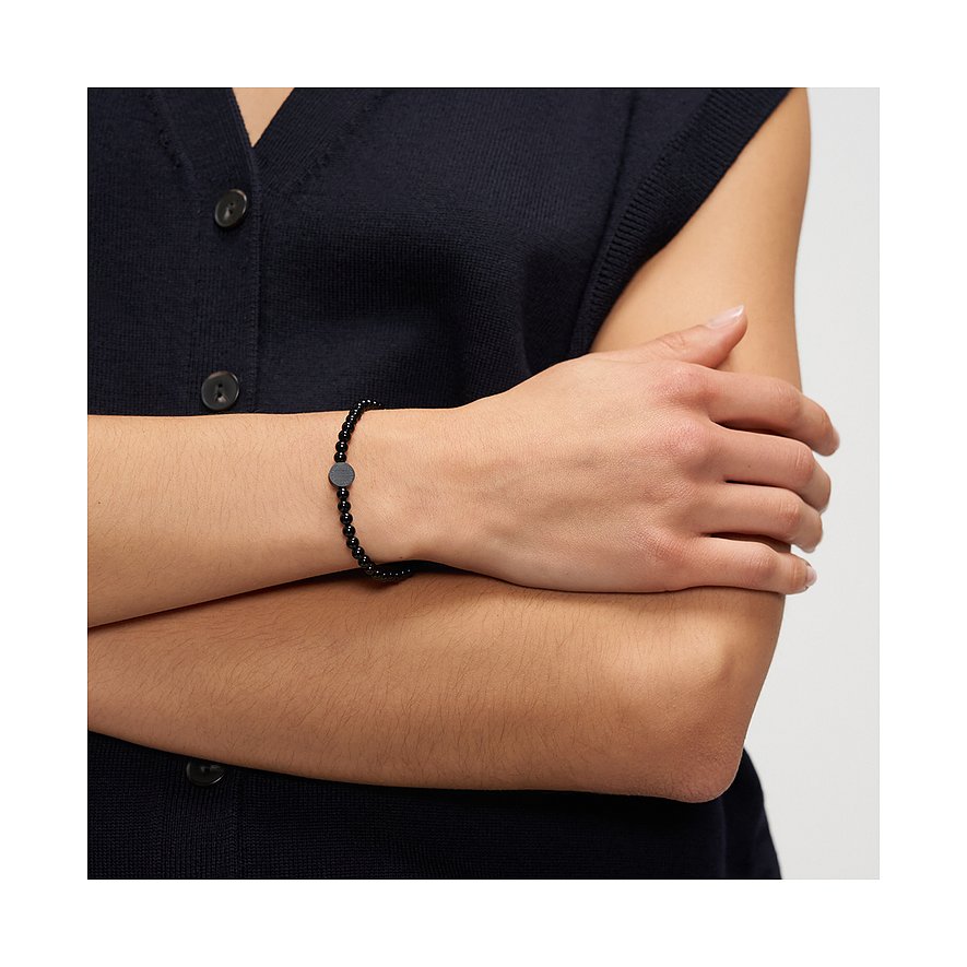 På en persons arm finns ett Liebeskind armbandsmycke i svart rostfritt stål med små pärlor och en rund platta.