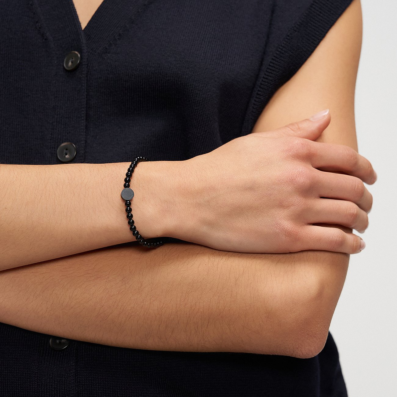 På en persons arm finns ett Liebeskind armbandsmycke i svart rostfritt stål med små pärlor och en rund platta.