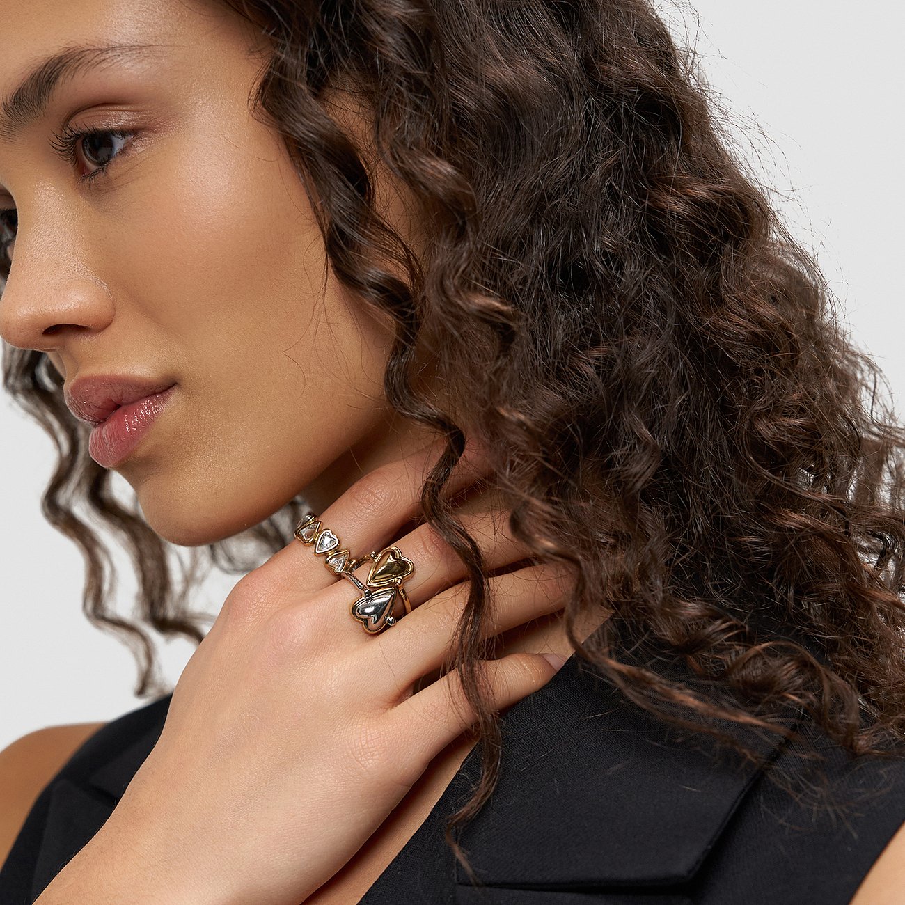Model trägt zweifarbigen Liebeskind Edelstahlring mit Herzdesign, blickt zur Seite. Gewelltes Haar fällt über ihre Schulter.
