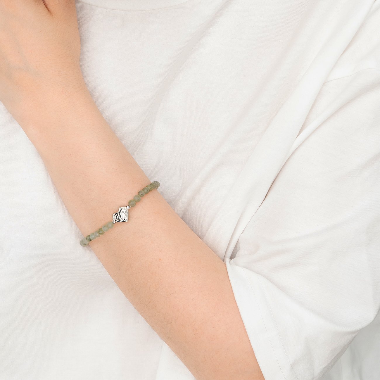 Am Arm getragenes Liebeskind Armband aus Edelstahl mit grünen Schmucksteinen und einem herzförmigen Anhänger.
