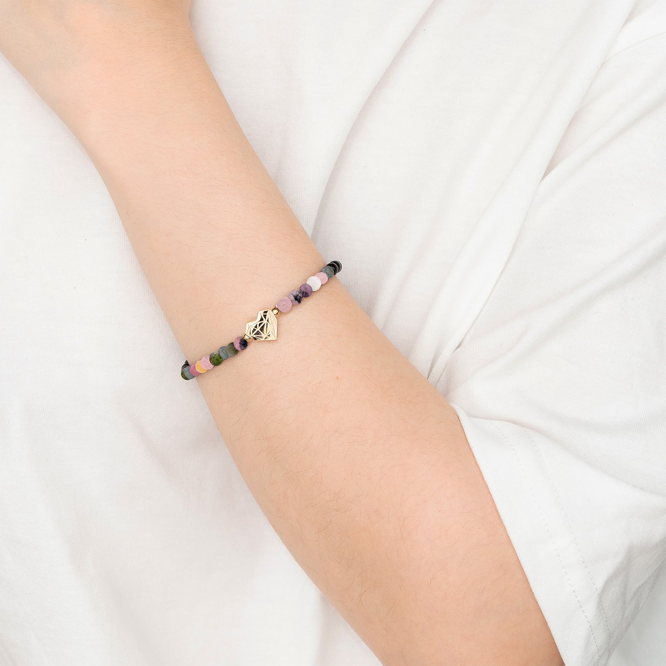 Liebeskind Armband aus Edelstahl mit bunten Perlen und goldfarbenem Logo-Anh nger an einem Arm.