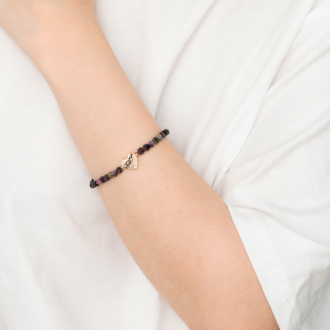 Liebeskind Armschmuck aus farbigen Perlen mit einem goldenen diamantförmigen Metallanhänger am Arm eines Models