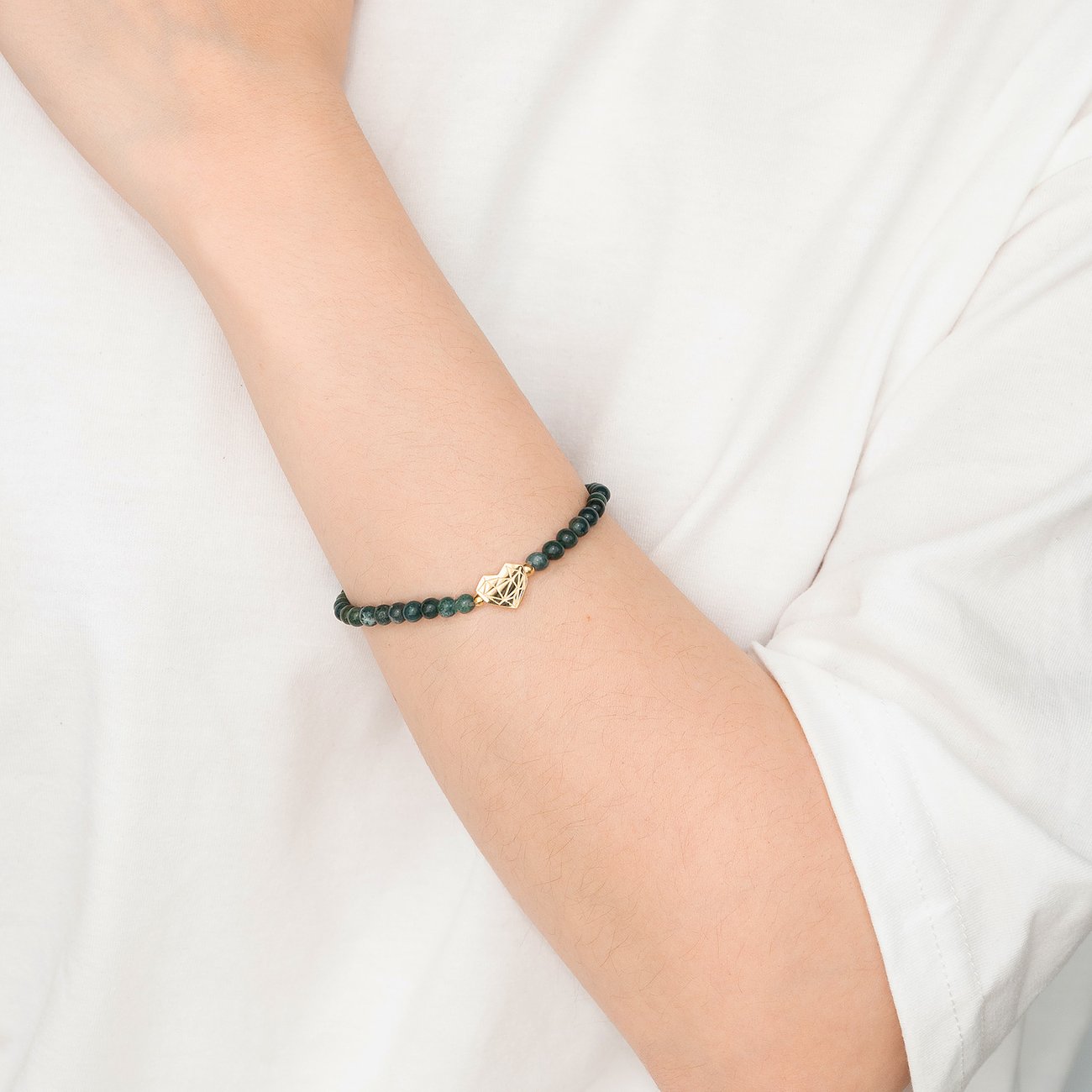 Am Arm getragenes Liebeskind Armband aus Edelstahl mit dunkelgrünen Perlen und einem goldenen Herz-Anhänger.