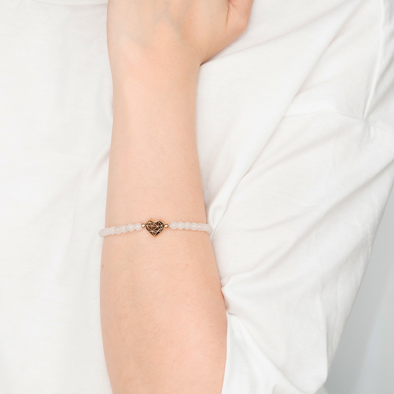 Liebeskind Armschmuck am Arm: zartes Perlenarmband mit herzförmigem Edelstahl-Detail in der Mitte.