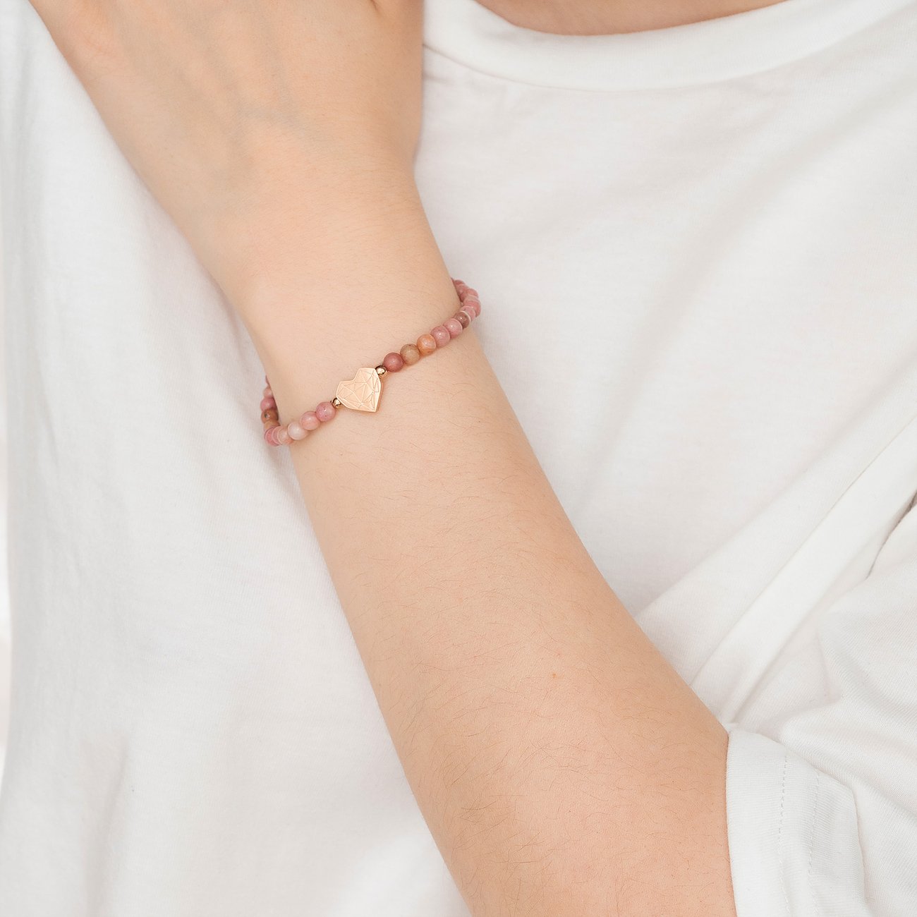 Ein Armschmuck von Liebeskind, bestehend aus mattrosa Steinperlen mit einem Anhänger aus goldfarbenem Edelstahl in Herzform.