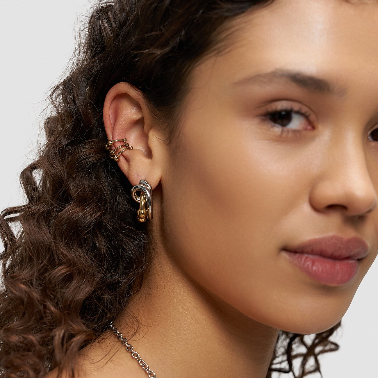 Nærbillede af en kvinde med et flerfarvet Liebeskind sæt af øreringe og earcuffs i rustfrit stål.