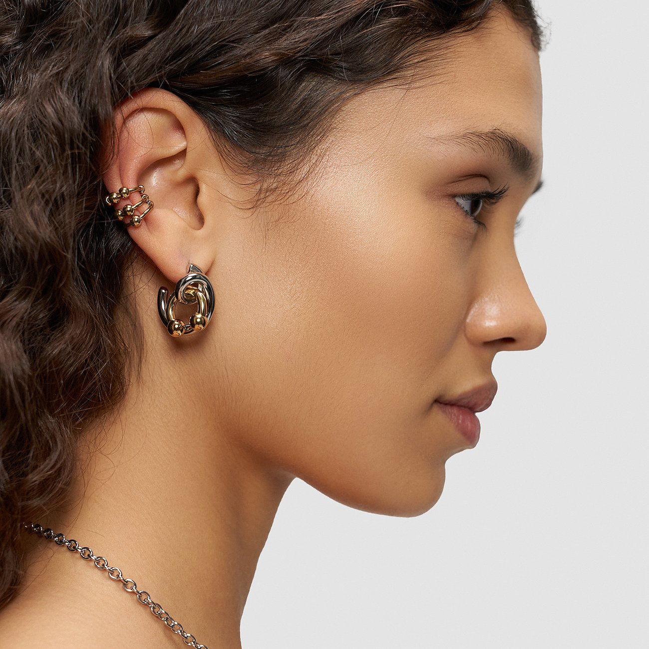 Model bærer Liebeskind smykkesæt i rustfrit stål, bestående af guld- og sorte øreringe og ear cuffs.