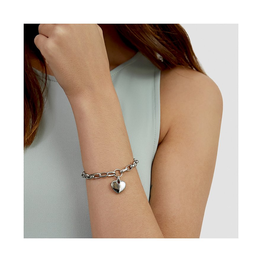 Ett glänsande s.Oliver armband i rostfritt stål med ett hjärtformat hänge syns på en kvinnas handled.
