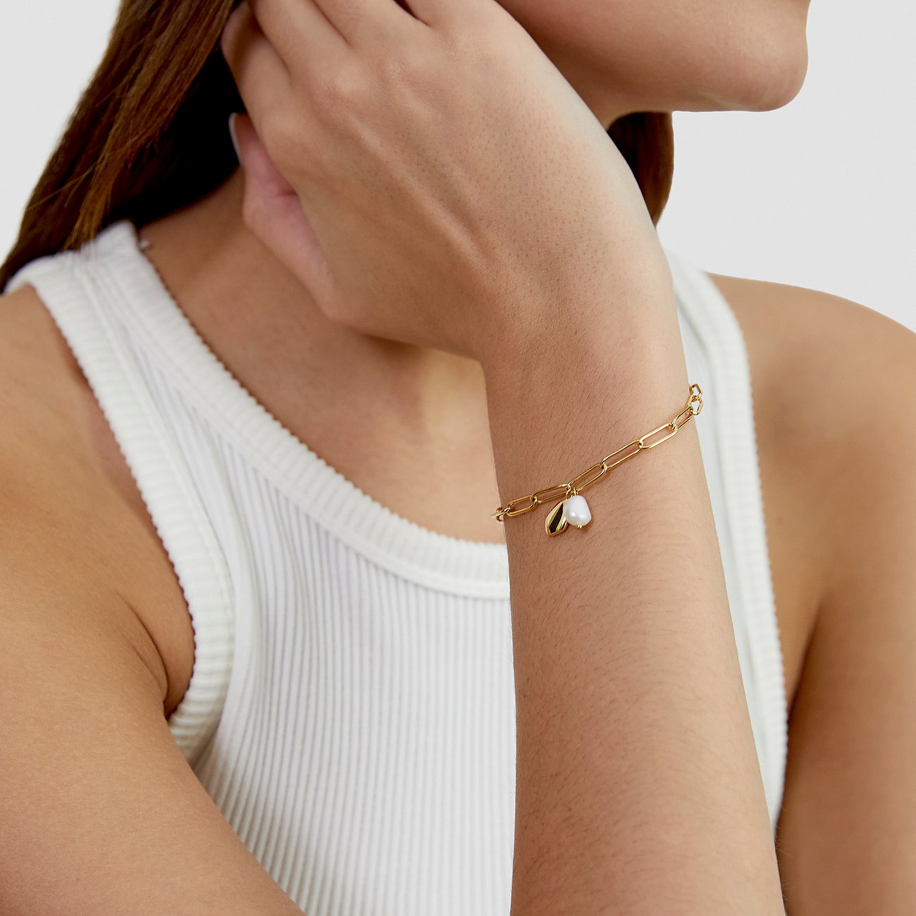 s.Oliver Armschmuck aus gelb-goldenem Edelstahl an einem Frauenarm, mit weißem herzförmigem Motiv.