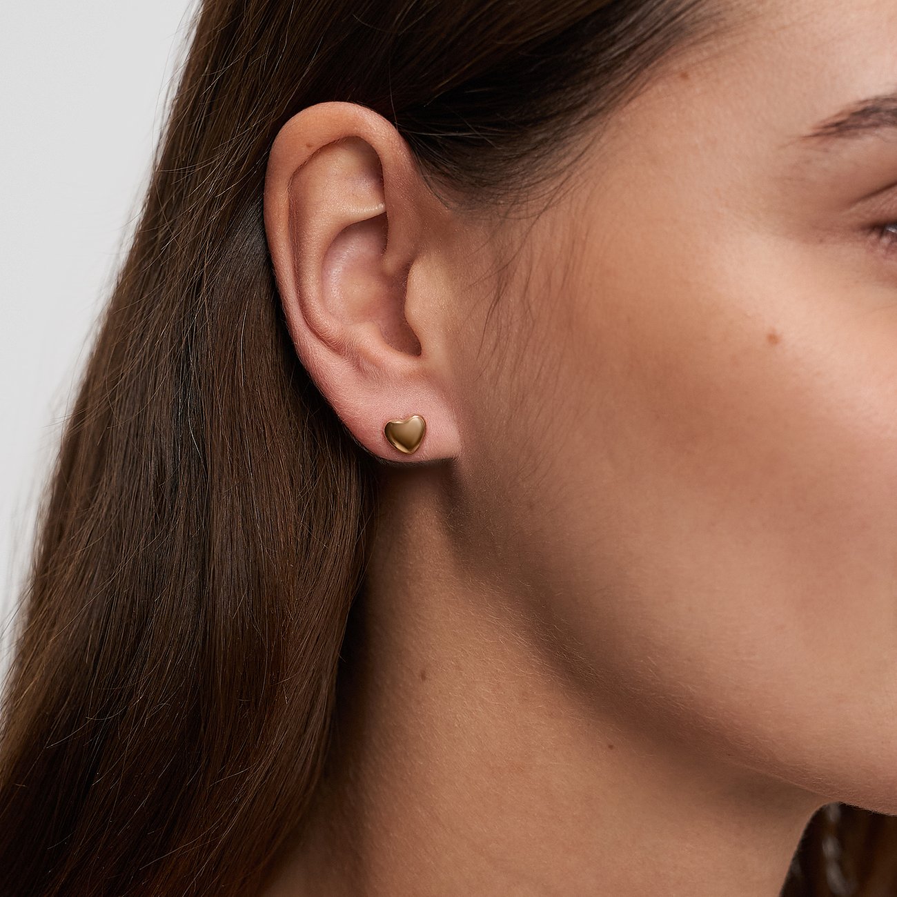 Gros plan d'une boucle d'oreille s.Oliver en forme de cœur en acier inoxydable doré, portée par un mannequin.