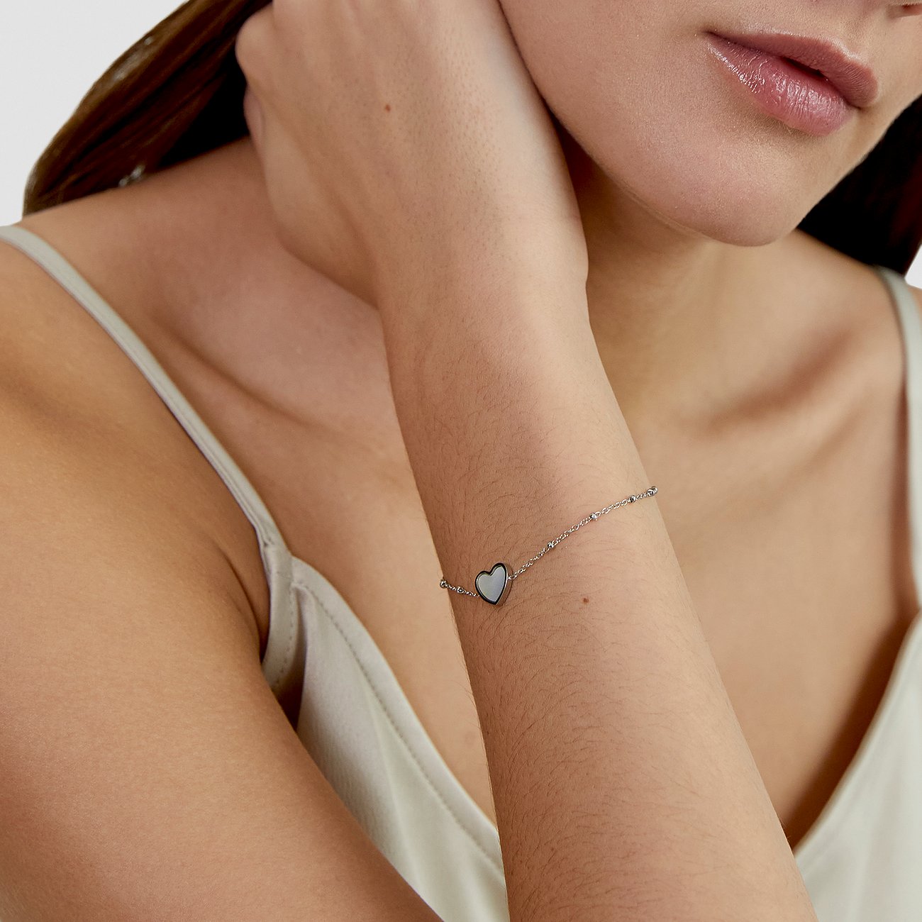 Am Arm einer Frau ist das s.Oliver Edelstahl-Armband mit einem Herz-Anhänger aus perlmuttfarbenem Stein zu sehen.