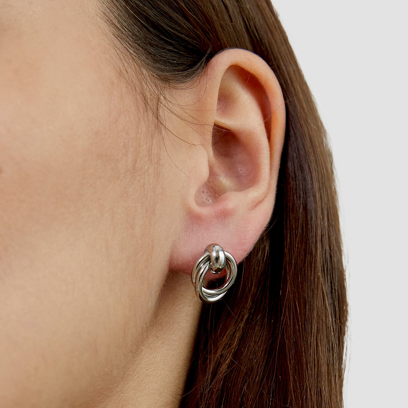 Ein s.Oliver Ohrschmuck aus Edelstahl, der drei ineinander verschlungene silberne Ringe am Ohrläppchen zeigt.