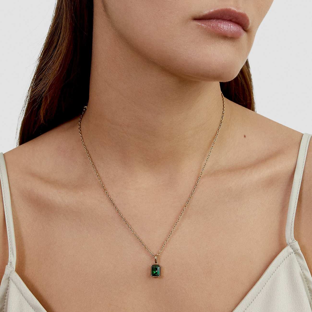 Ein s.Oliver Halsband aus goldfarbenem Edelstahl mit einem rechteckigen Zirkonia in Smaragdgrün, getragen von einem Model.