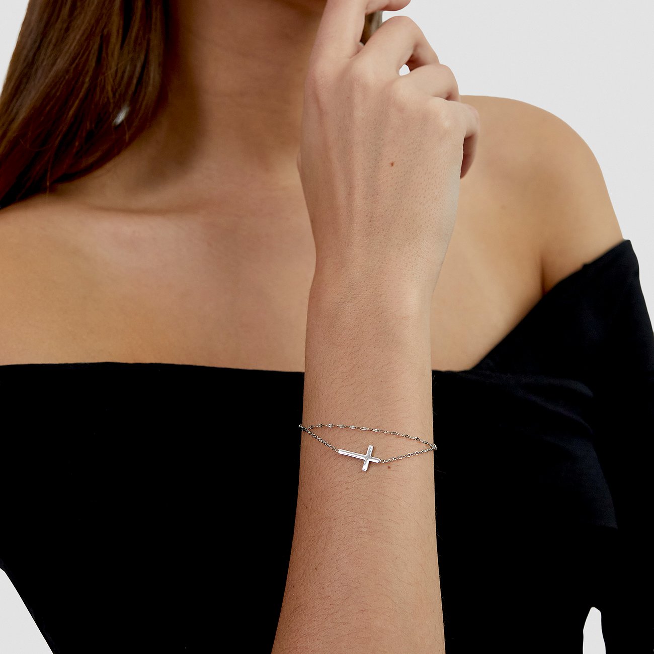 Am Handgelenk einer Frau ist ein s.Oliver Armschmuck aus Edelstahl mit Kreuz-Anhänger zu sehen.