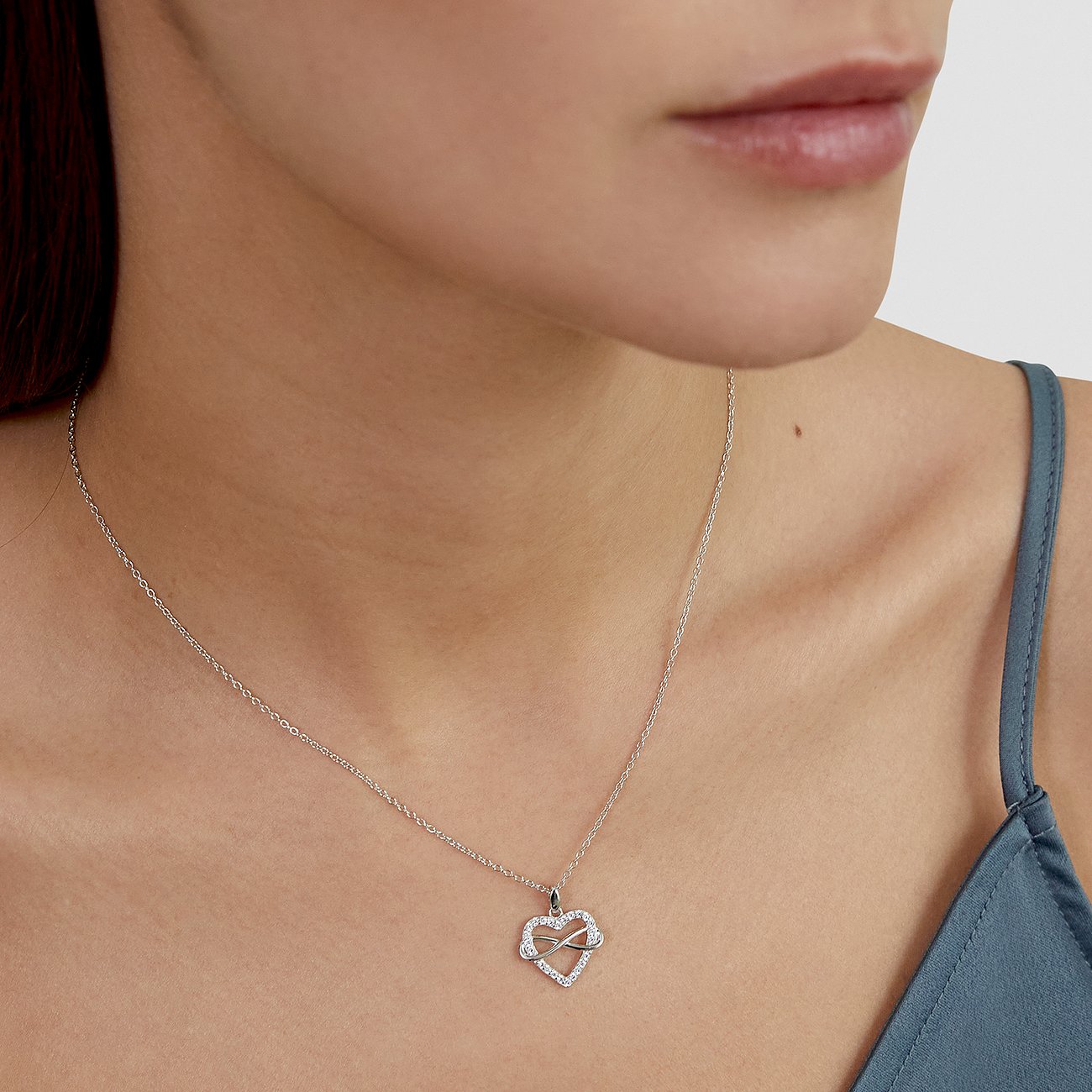 En kvinna bär ett silverfärgat s.Oliver-halsband med ett hjärtformat hänge, dekorerat med zirkoniafärgade stenar.