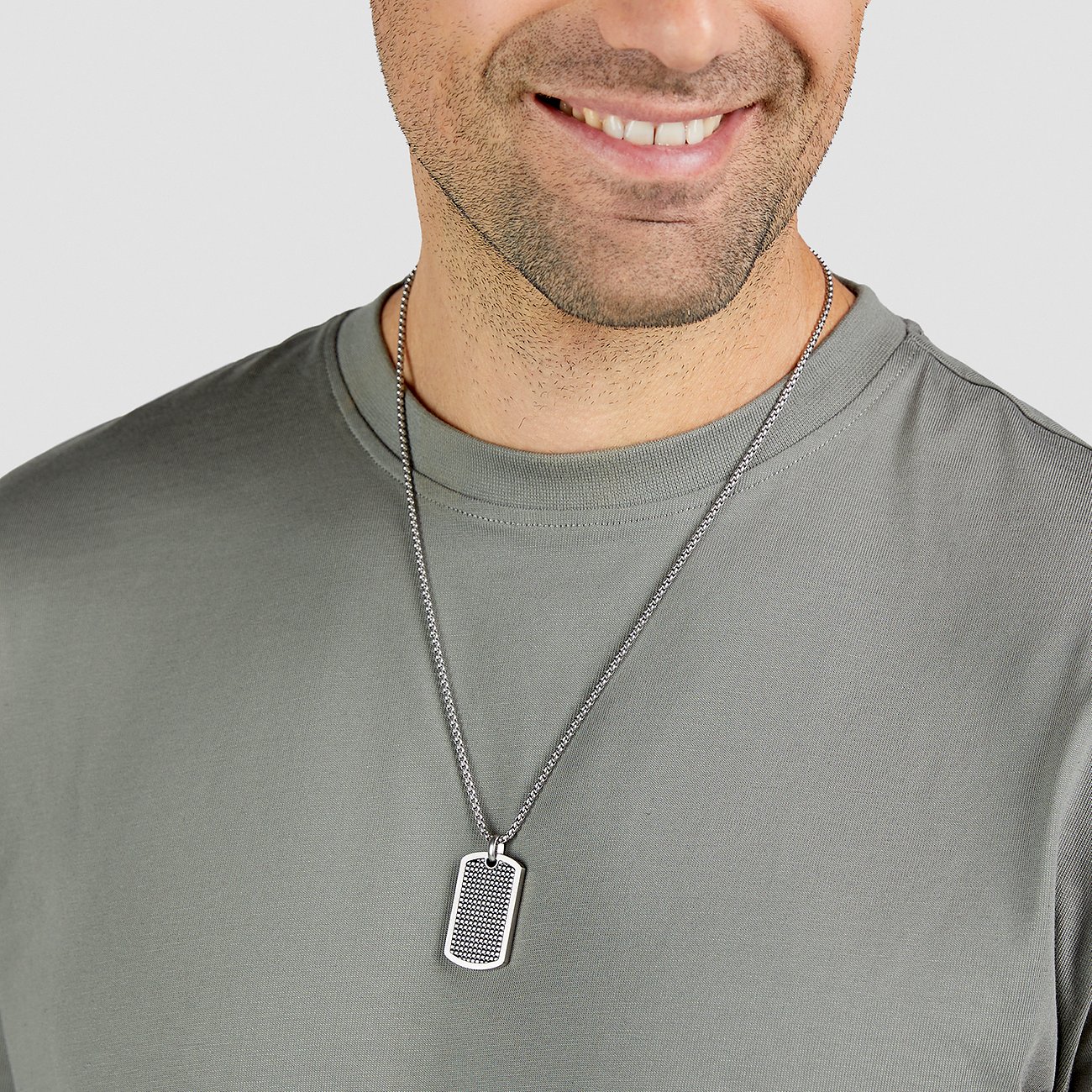 Närbild av en leende man som bär ett s.Oliver halsband i rostfritt stål med dog-tag hänge.