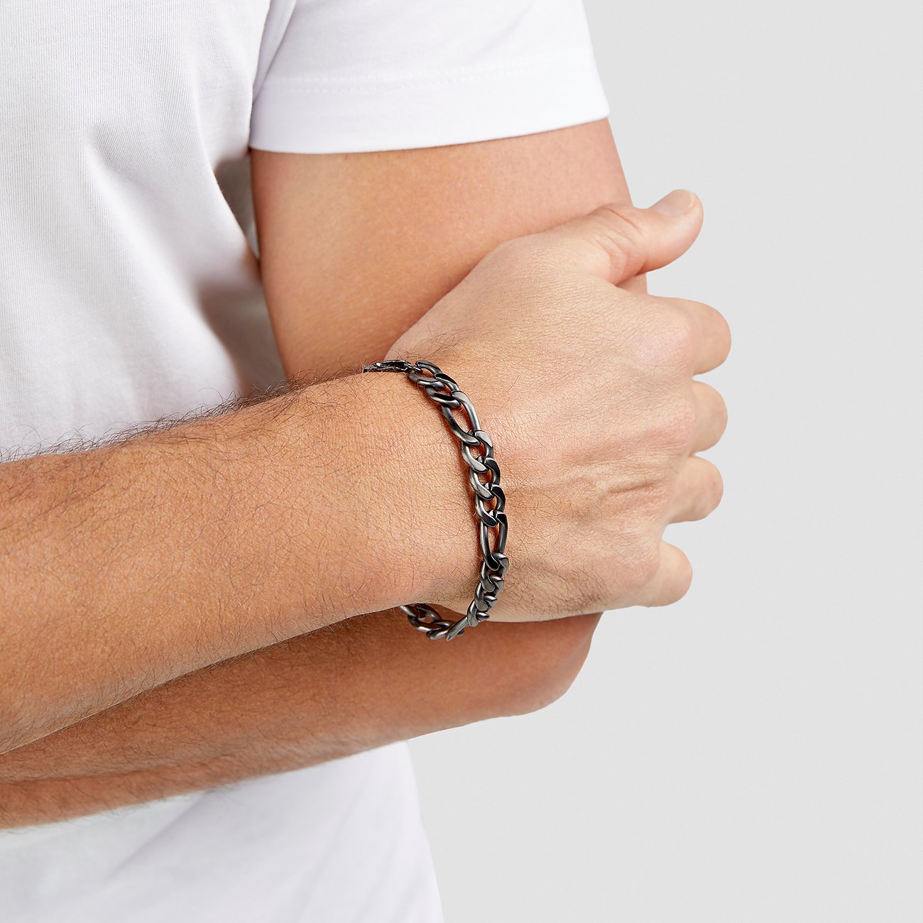 En man med ett s.Oliver armband i pansarkedjedesign av mörkt rostfritt stål på sin underarm.