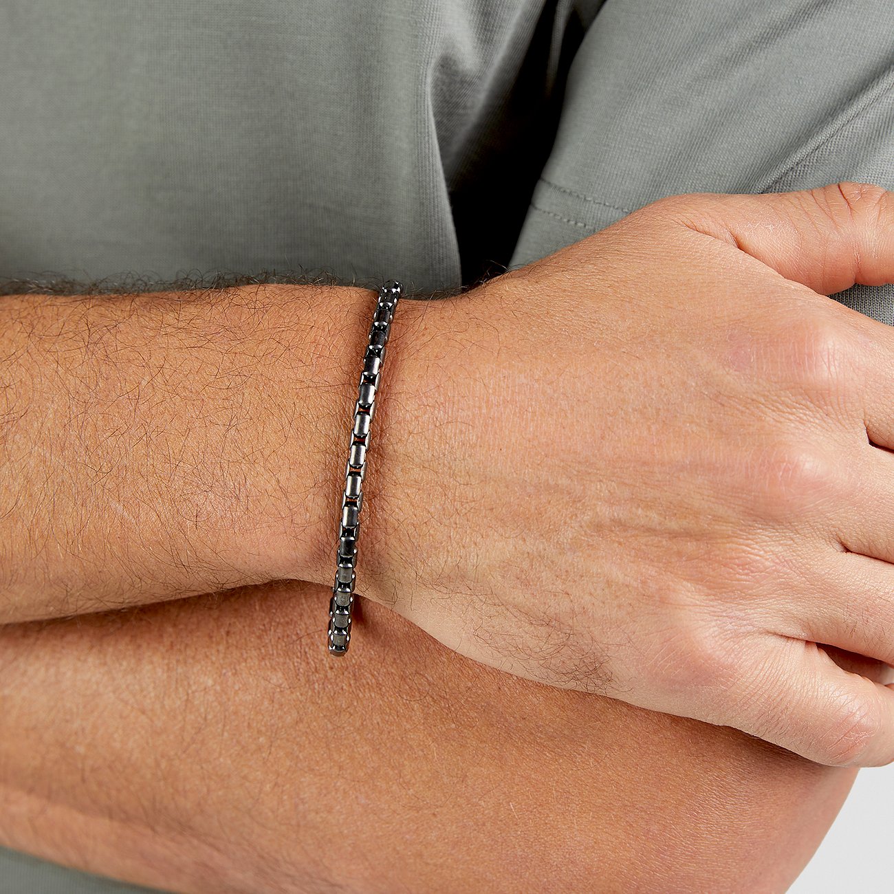 Ett s.Oliver armband i mörkt rostfritt stål med glänsande länkar syns på en mans handled.